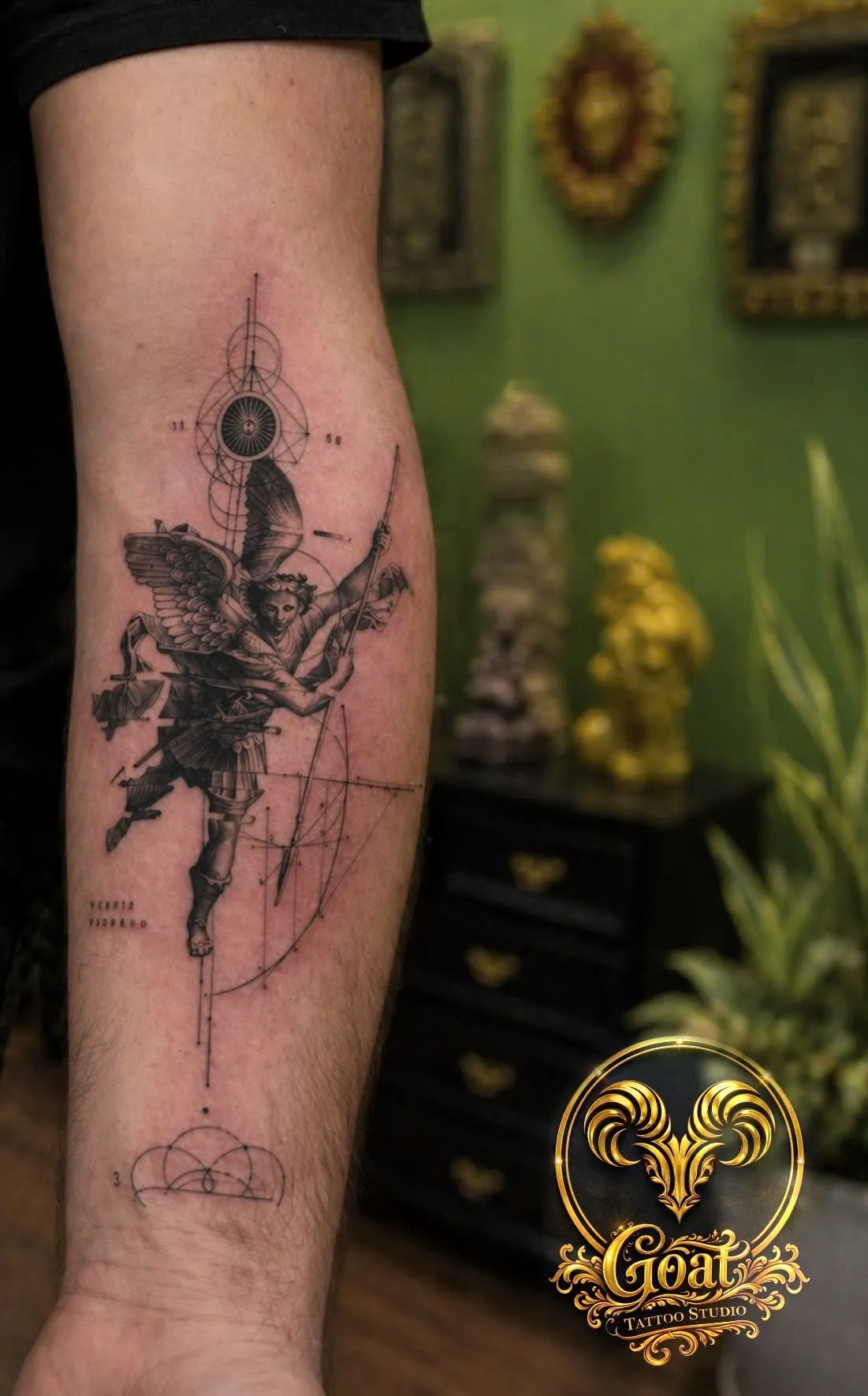 Black and grey winged angel warrior tattoo with geometric compass details on the forearm, by GOAT Tattoo Studio Hanoi.